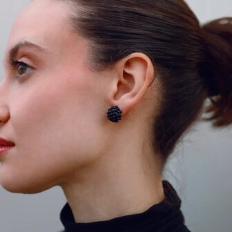 Persoon draagt kleine gouden bol oorstekers met kraalstructuur