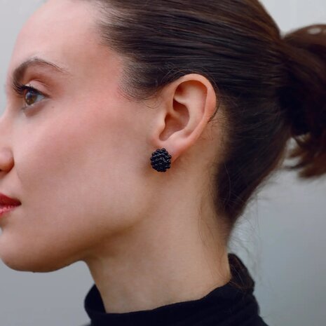 Persoon draagt zwarte bol oorstekers van glaskralen klein formaat