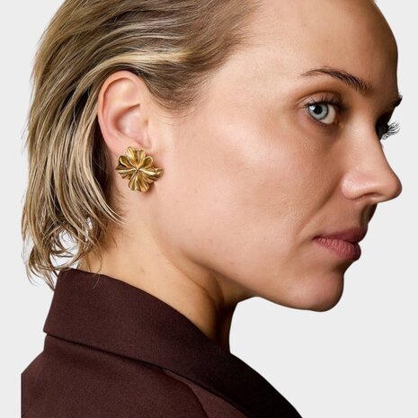 Persoon draagt gouden bloem steker oorbellen detail